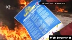 Жұмысшы киіміндегі адам президентшіл «Нұр Отан» партиясының плакатын отқа тастап жатыр. Жаңаөзен, 16 желтоқсан, 2011 жыл. (К+ телеарнасы бейнехабарынан алынған скриншот).